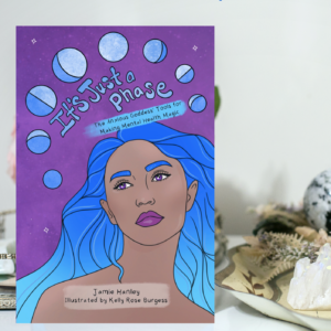 A picture of a purple workbook and a woman with blue hair looking up at the phases of the moon with a Book title of "It's Just a Phase: The Anxious Goddess Tools for Mental Health Magic"